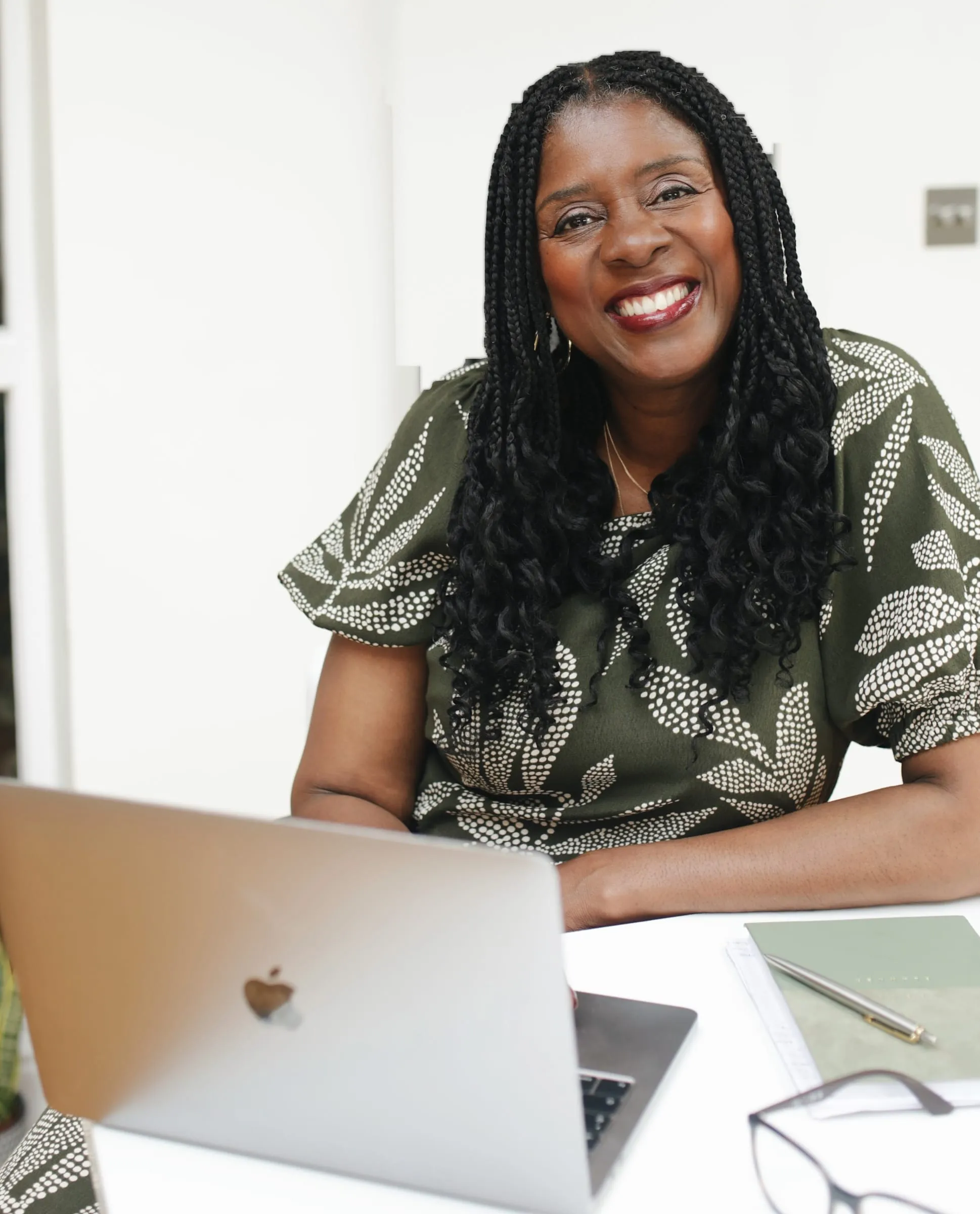 Lorraine Lee smiling at a desk with a laptop, notebook and glasses