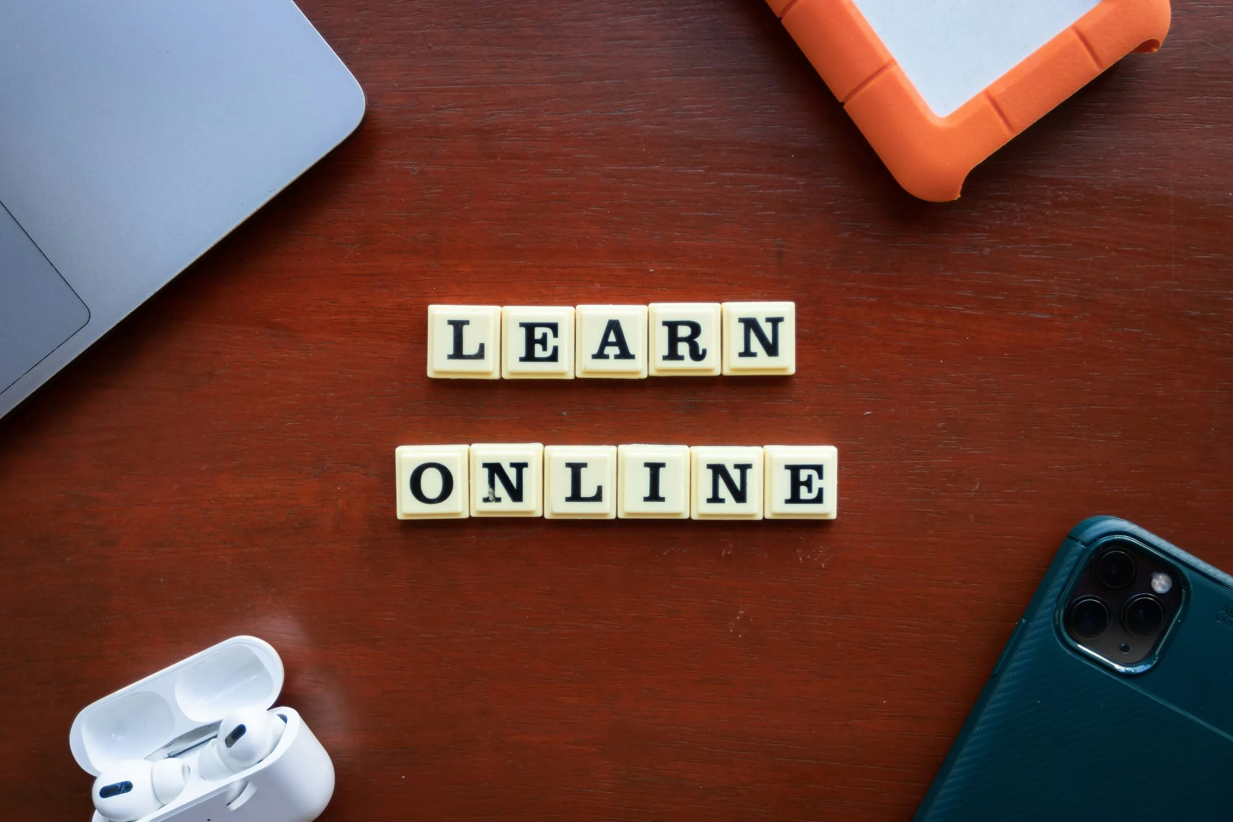 Letter tiles spelling "learn online" beside a laptop and phone