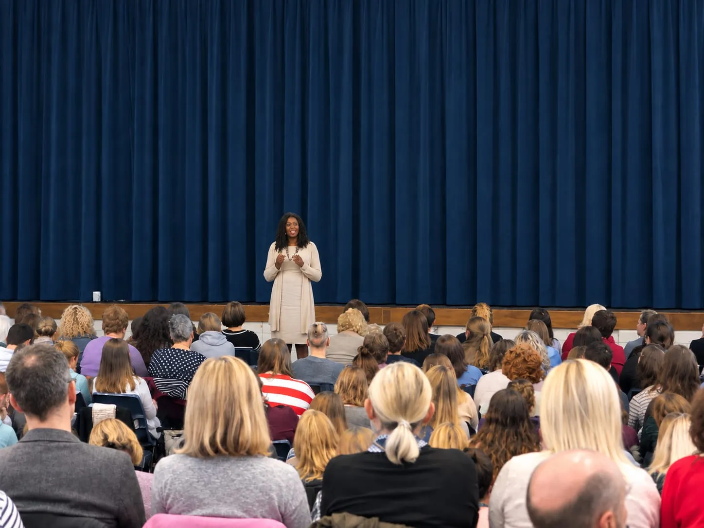 Lorraine speaking to a hall full of parents in front of blue stage curtains