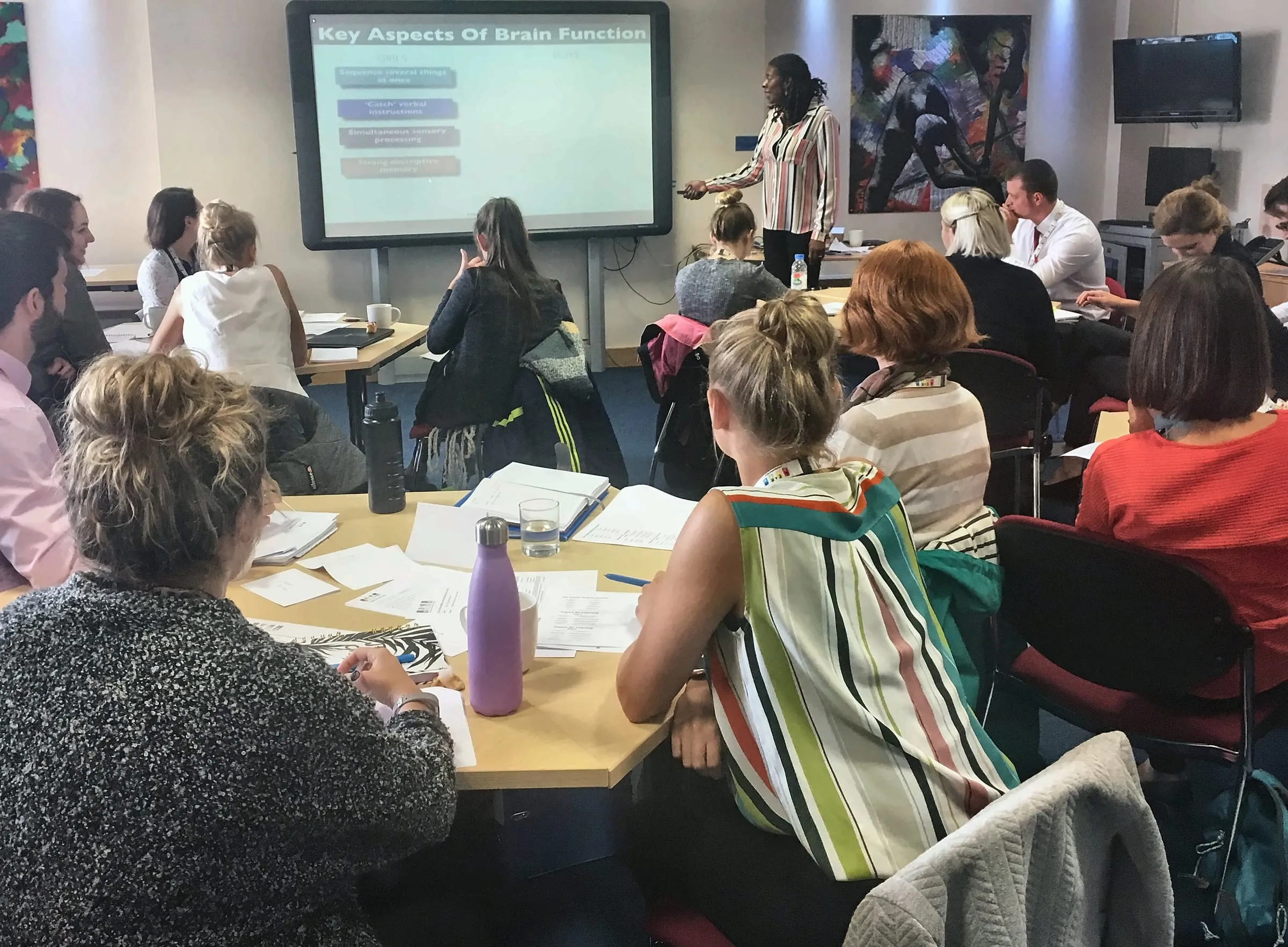 Lorraine Lee leading a staff training session, teachers at tables in front of a screen about brain function